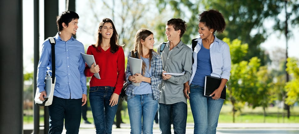 Five happy college students walking across campus