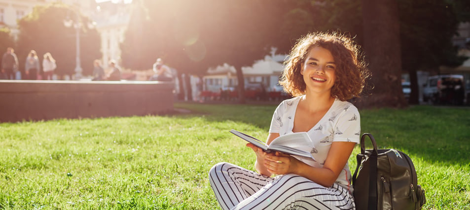 female student sitting outside on grass on college campus